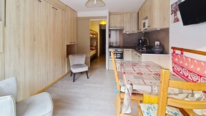 A compact kitchen with wooden cabinets, a microwave, and a sink. There is a dining table with chairs and a patterned tablecloth. - Portes Du Soleil PSA46 TELECABINE & MOUNTAIN 4 Per (Châtel)