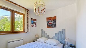Un dormitorio con cama, ventana, radiador y dos lámparas fijadas a la pared.