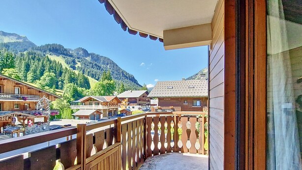 Un balcón de madera con vistas a un pueblo de montaña y un restaurante llamado "LES PIERREUS".