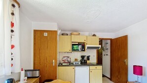 Una cocina compacta con armarios de madera, microondas, cafetera y un refrigerador pequeño.