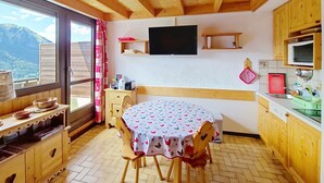 Una cocina acogedora con armarios de madera, una mesa de comedor con sillas, un televisor montado en la pared y un ventanal con vistas a la monta ña.