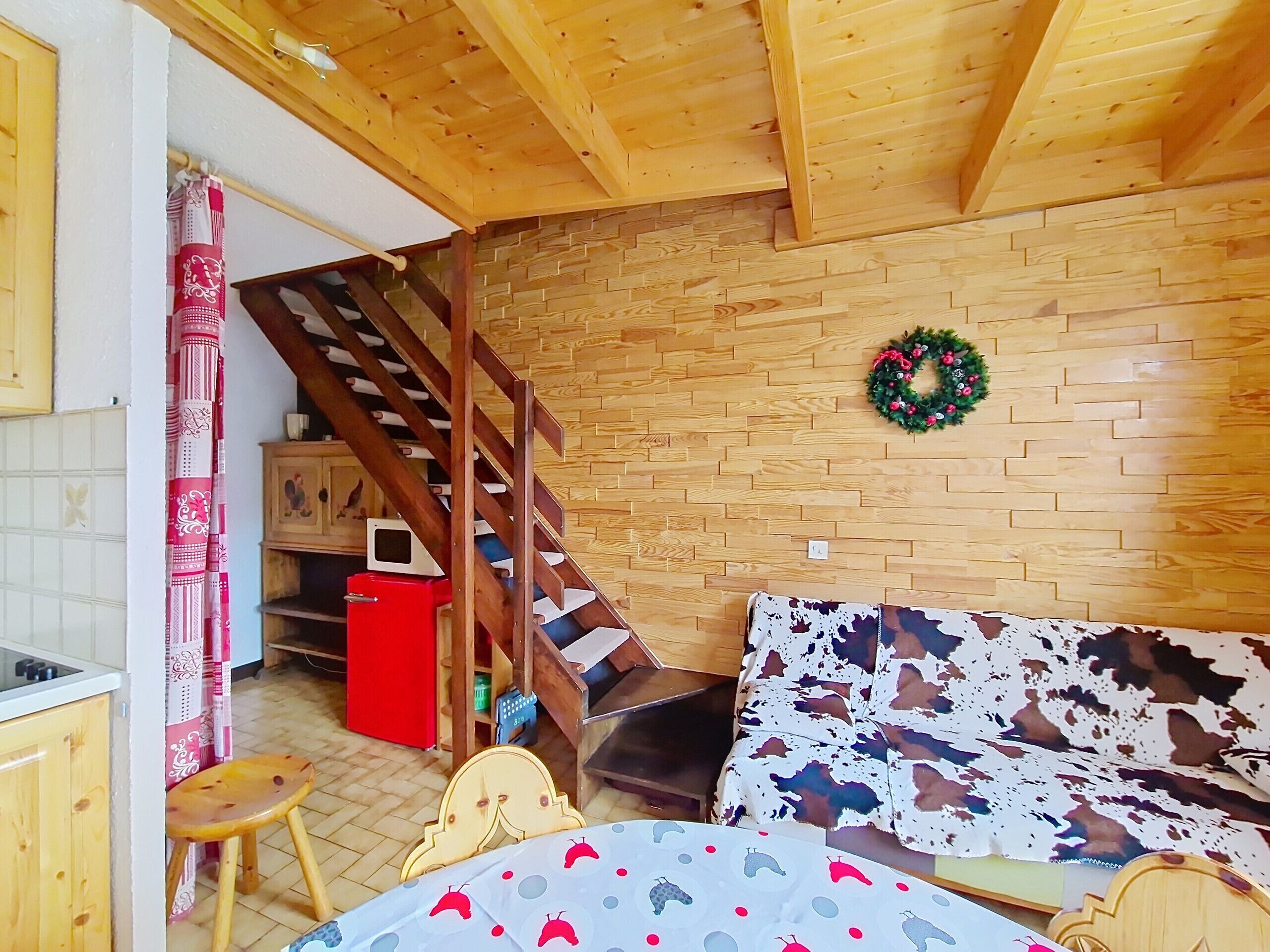 A cozy room with a wooden ceiling, a staircase, a brick wall, and a small table with a patterned tablecloth.