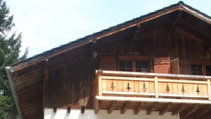 A wooden chalet with a balcony decorated with tree motifs, a garage, and bicycles parked outside.