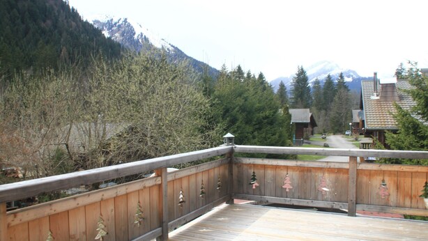 A wooden deck with railings, overlooking a forested area and a mountain range.