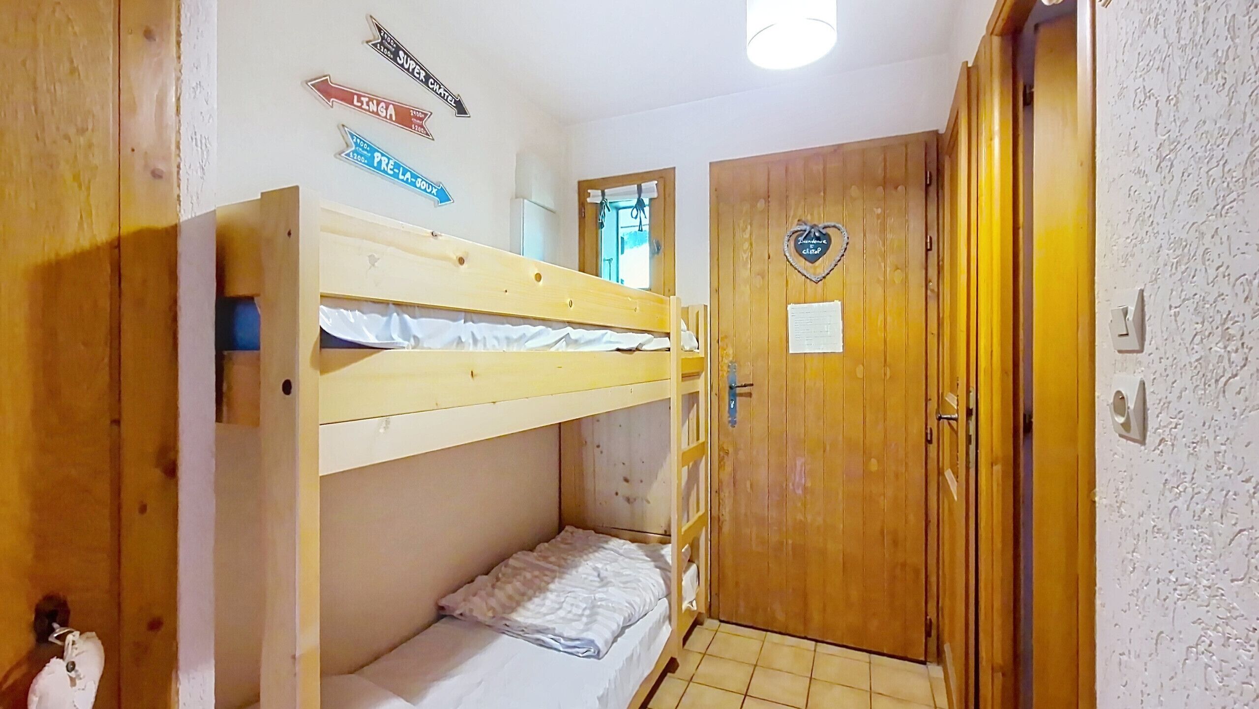 A room with a bunk bed, a wooden door with a heart-shaped plaque, and wall signs indicating directions to nearby locations.