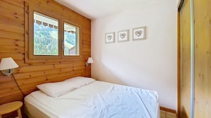 Une chambre aux murs lambrissés, avec un lit, deux lampes de chevet et une fenêtre donnant sur des arbres.