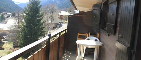 Un balcon doté d’une balustrade en bois, d’une petite table et de deux chaises. On aperçoit une vue sur les montagnes en arrière-plan.