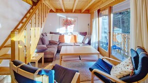 A cozy cabin interior with a wooden ceiling, a sofa set, a dining table, and a large window offering a view of the outdoors. - Myrtilles MR27 TELECABINE & NATURE 6 pers. (Châtel)