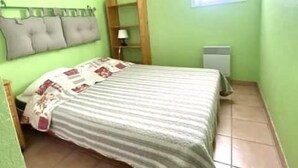 Una camera da letto piccola e luminosa, con un letto, un comodino, una finestra e un termosifone.