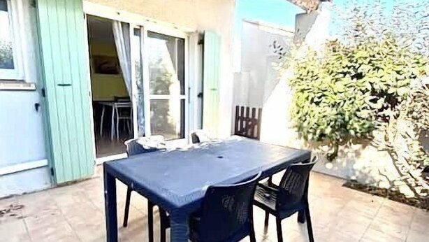 Una terrazza all'aperto con tavolo e sedie, un pergolato sopra e vista su un giardino.