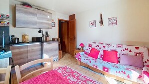 Ein gemütlicher Wohnbereich mit einer Küchenzeile, einem Sofa mit festlicher Bettwäsche und einem Essbereich mit einem Stuhl.