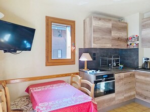Una cocina compacta con armarios de madera, horno integrado, microondas y un pequeño comedor con mesa y sillas.