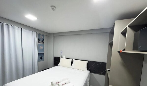 Una habitación de hotel con una cama, un televisor sobre un mueble bajo y un estante fijado a la pared.