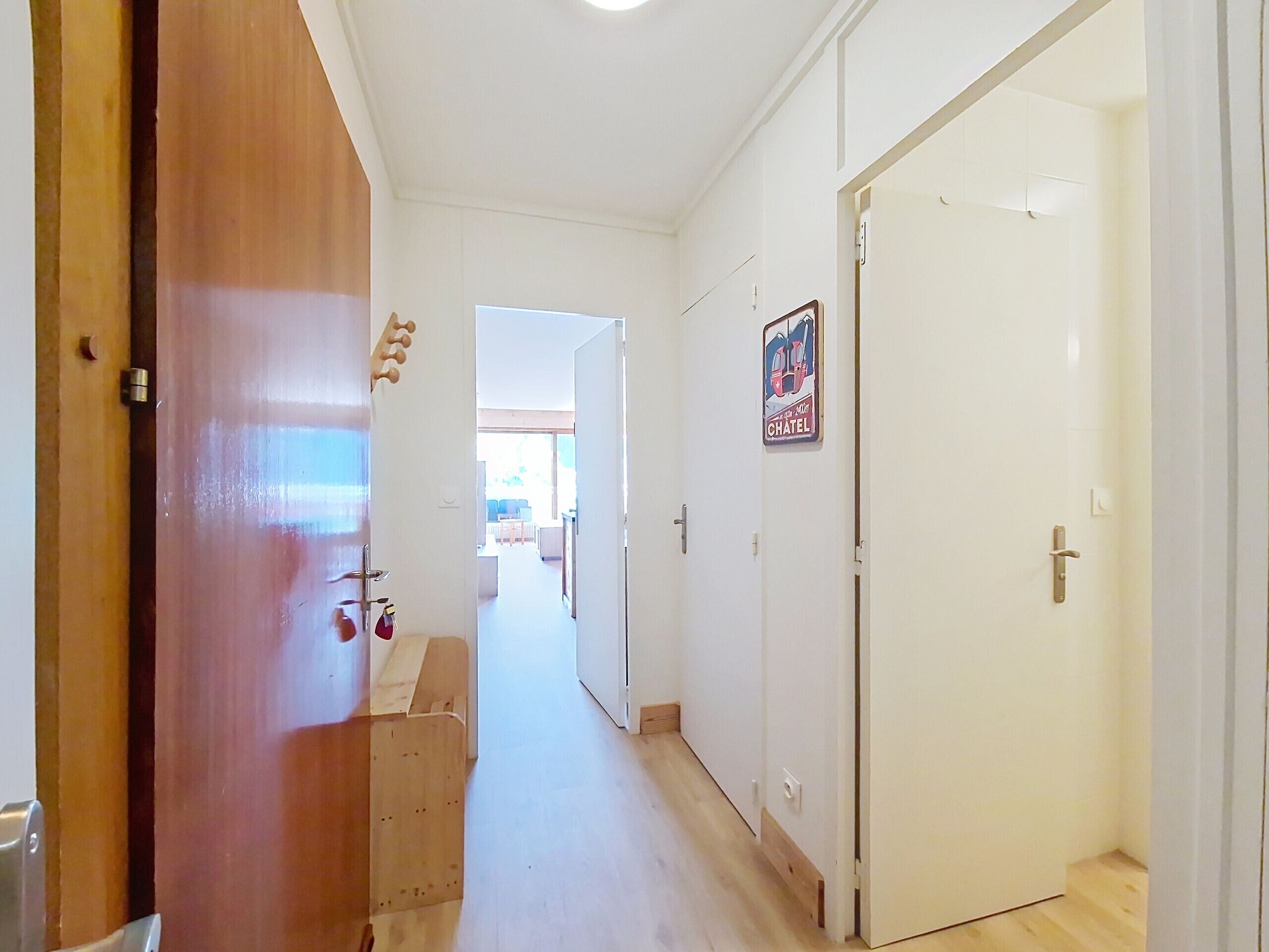 A hallway with a wooden door on the left, a white door on the right, and a poster on the wall.