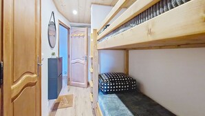 A narrow hallway with a bunk bed, wooden wardrobe, and a door with a mirror.