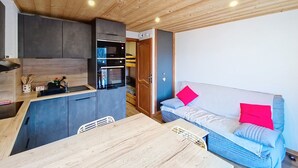A compact kitchen with modern appliances, a dining table, and a sofa with red pillows.
