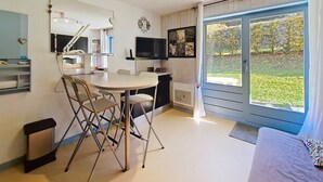 A modern kitchen with a dining area, a TV, and a large window with a view of a garden. - Campanules CP6 TELECABINE & NATURE 4 Pers (Châtel)