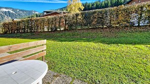 A grassy outdoor area with a wooden bench and a table, surrounded by a hedge and a mountain backdrop. - Campanules CP6 TELECABINE & NATURE 4 Pers (Châtel)