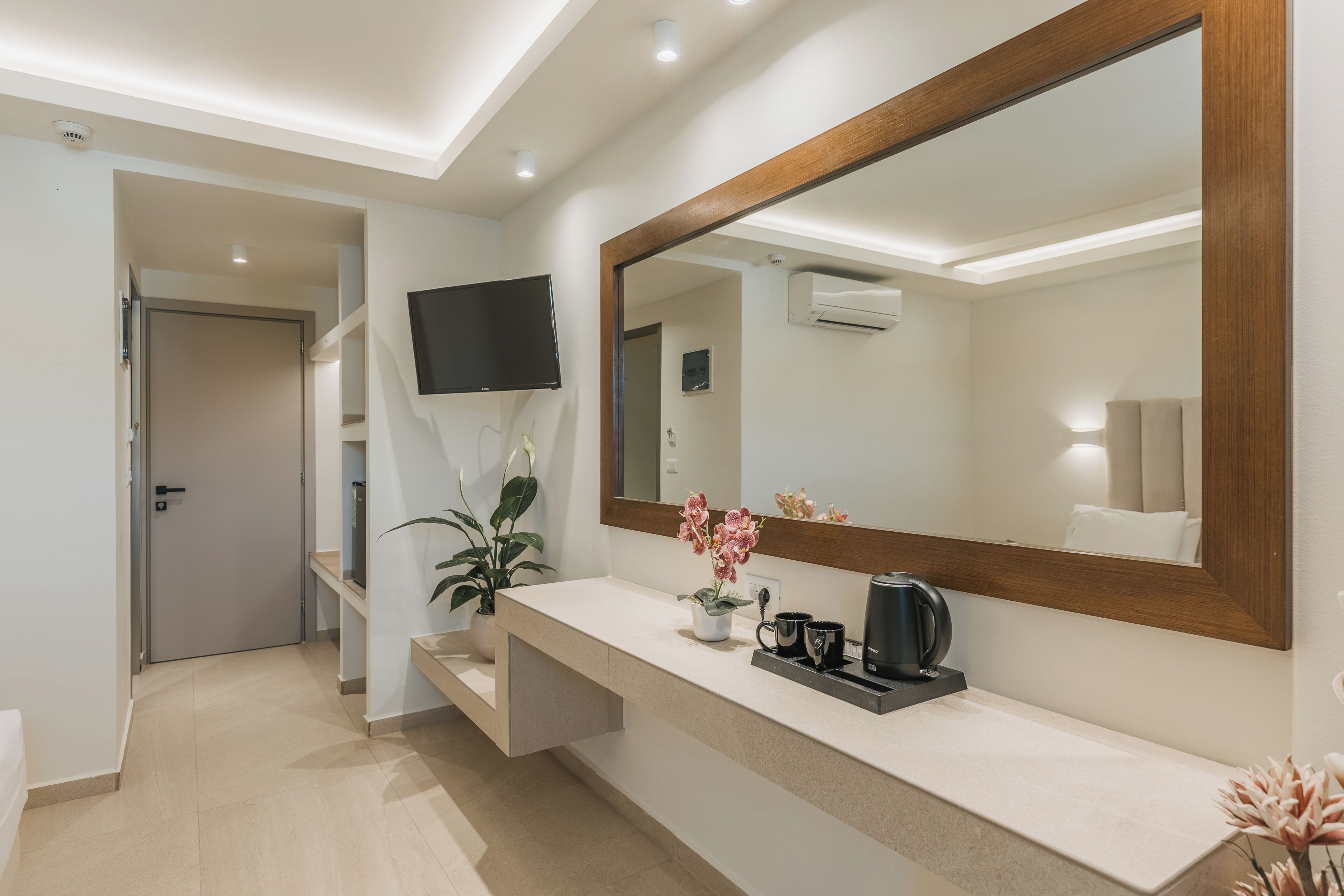 A modern bathroom with a large mirror, a sink, a potted plant, and a flat-screen TV mounted on the wall.
