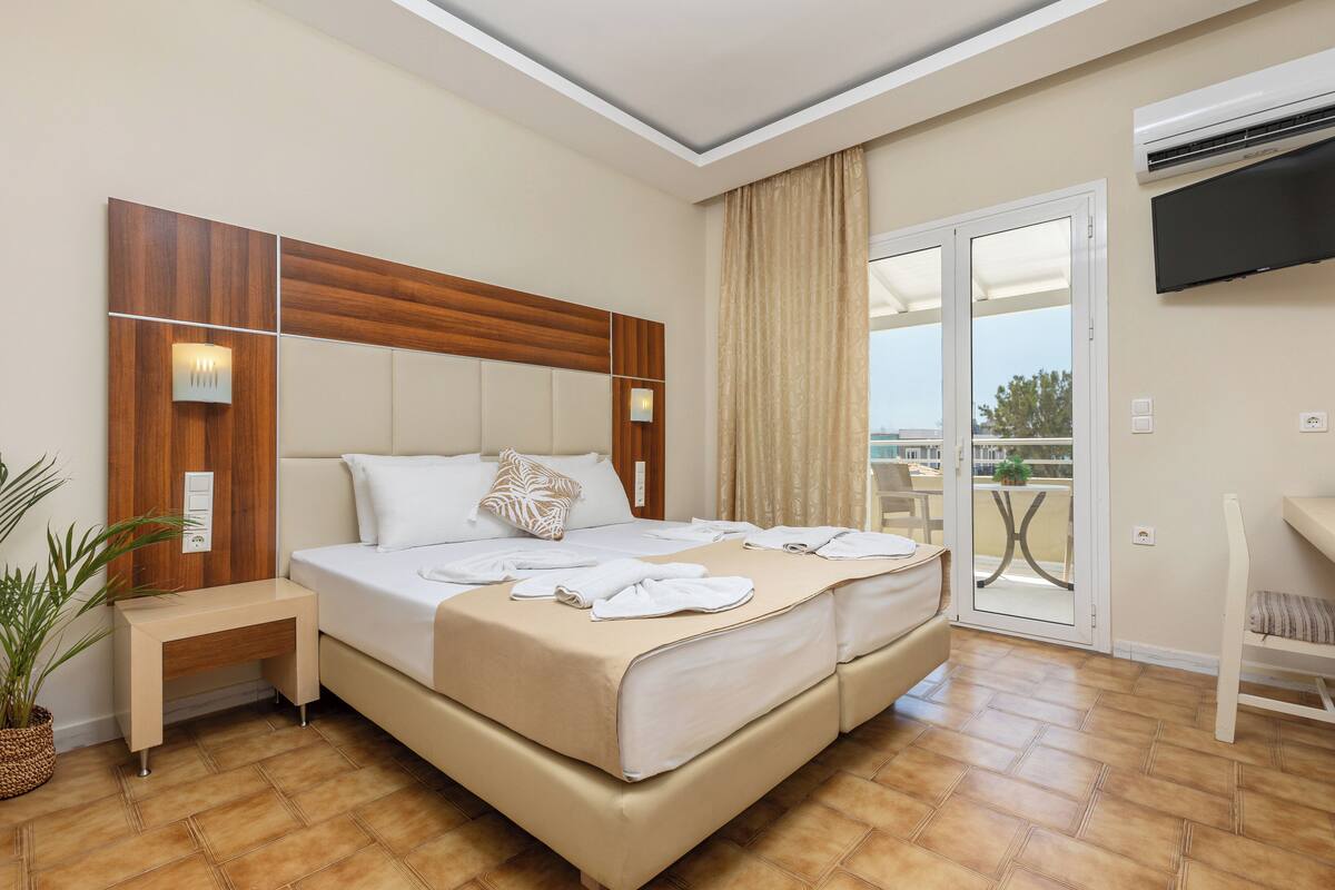 A hotel room with a large bed, a bedside table, a TV mounted on the wall, and a sliding glass door to the balcony.