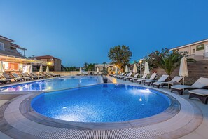A swimming pool with lounge chairs and umbrellas, surrounded by buildings. - Esperia Hotel (Zakynthos)