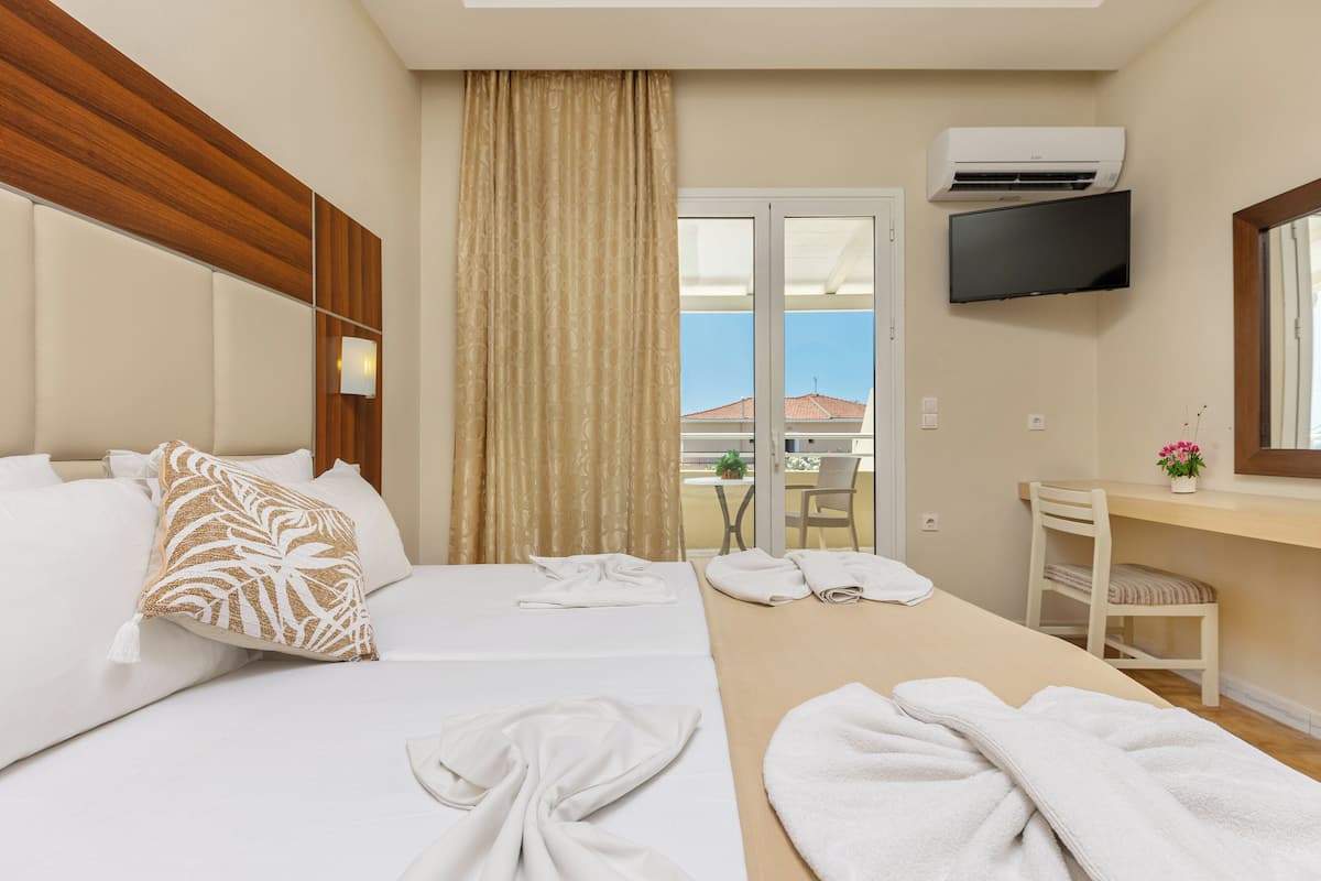 A hotel room with two beds, a desk, a chair, a TV, and an air conditioning unit.