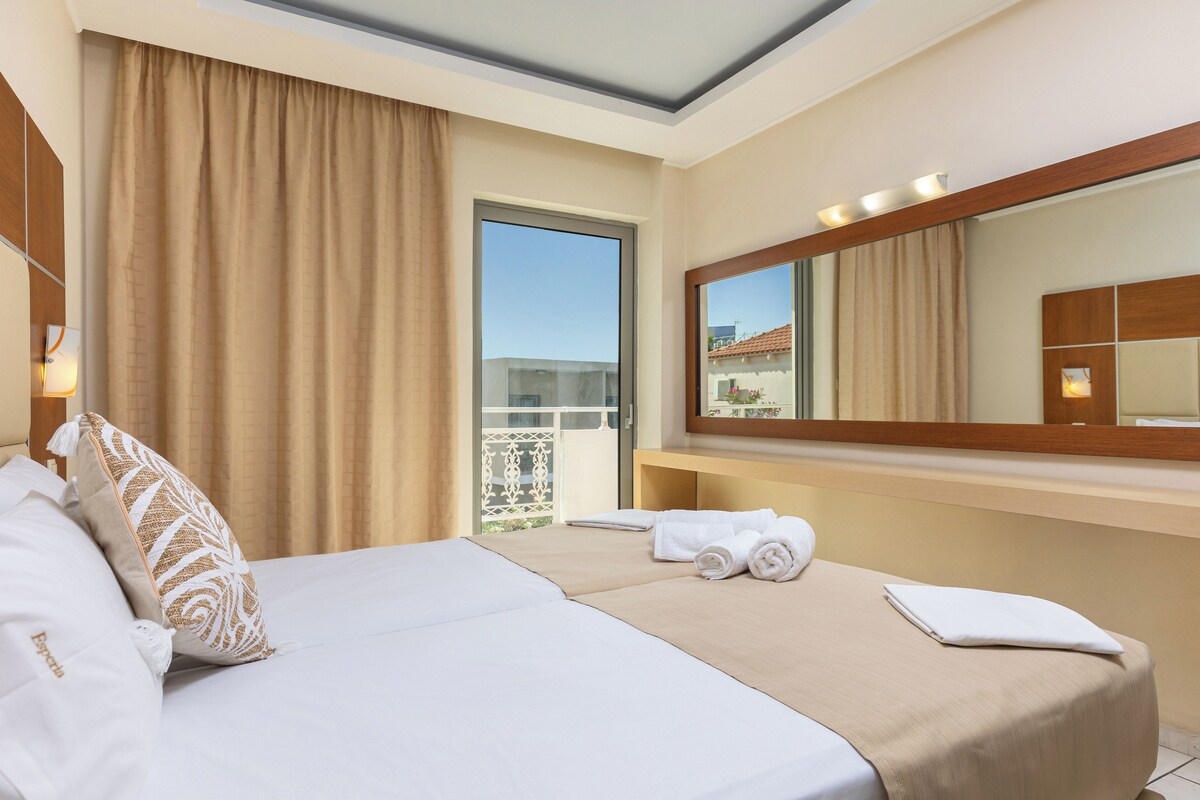 A hotel room with a bed, a large mirror, a window with curtains, and a balcony view.