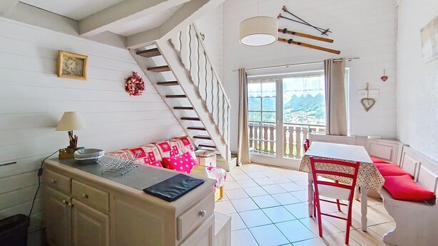Ein gemütliches Zimmer mit Küchenzeile, einem Esstisch mit Stühlen, einer Treppe und einem Balkon mit schöner Aussicht.