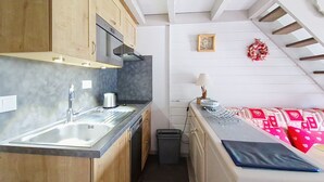 Eine kompakte Küche mit Holzausziehtüren, einem Edelstahlspülbecken und einer Mikrowelle. Auf der Arbeitsplatte befindet sich ein kleiner Mülleimer und eine Steckdose.