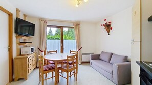 Un espacio habitable compacto con una mesa de comedor, sillas, un sofá, un televisor de pantalla plana, microondas y un adorno de pared.