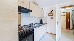 Una cocina compacta con estufa, horno y pileta, muebles de madera y un pequeño estante de madera.
