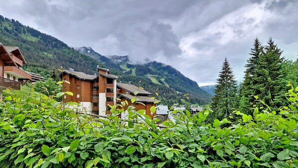 Un edificio de estilo chalé de madera con balcones, rodeado de vegetación exuberante y montañas al fondo.