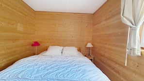 Una habitación con paredes de madera, una cama con ropa blanca, dos lámparas de noche y una lámpara roja a la izquierda.