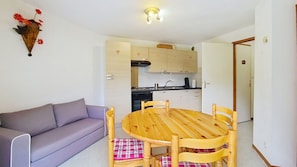 Un espacio habitable pequeño con sofá, mesa de comedor de madera con sillas, zona de cocina y un aplique de pared.