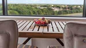 Une table en bois sur laquelle est disposée une assiette de fruits, placée devant une fenêtre donnant sur un paysage verdoyant.