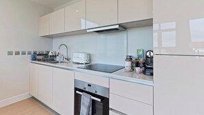 Une cuisine moderne avec des armoires blanches, une hotte de cuisinière en acier inoxydable, un four encastré, un évier et une machine à café.