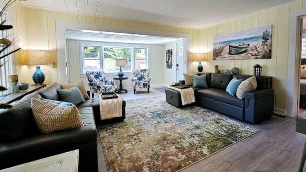 A spacious living room with a large window, a fireplace, and a cozy seating area. - Vintage charm, modern comfort! Lakeshore retreat 3 mins to the beach! (Muskegon)