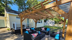 An outdoor patio area with wicker furniture and a pergola structure. - Vintage charm, modern comfort! Lakeshore retreat 3 mins to the beach! (Muskegon)
