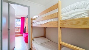 A bunk bed room with a wooden frame, white bedding, and a pink chair.