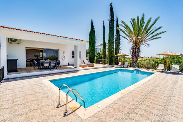 Una piscina con solárium azulejado, sillas de descanso y zona de comedor con mobiliario exterior.