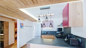 A modern kitchen with wooden cabinets, a built-in oven, and a microwave. There are hanging pendant lights and a small island with a sink. - VERONICA VR51 NATURE & MOUNTAIN 5 Pers (Châtel)