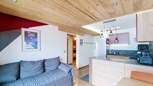 A modern interior with a grey sofa, wooden ceiling, kitchen area with appliances, and a small dining table. - VERONICA VR51 NATURE & MOUNTAIN 5 Pers (Châtel)