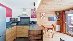 A compact kitchen with wooden cabinets, a microwave, and a coffee maker. There is a dining area with a table and chairs, and a TV mounted on the wall. - VERONICA VR51 NATURE & MOUNTAIN 5 Pers (Châtel)