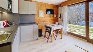 Et moderne køkken med træindretning, et spiseområde med bord og stole, samt et stort vindue der giver udsigt til naturen.