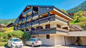 A multi-story building with balconies, a car parked in front, and a mountainous backdrop. - Biches BIA17 MOUNTAIN & QUIET 4 Pers. (Châtel)
