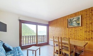 A room with a wooden paneled wall, a dining table with chairs, a small white table, and a sofa. - Tavaillons TV31 SWIMMING POOL & CENTER 4 Pers (Châtel)