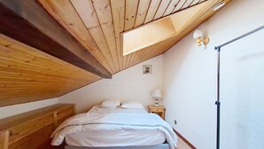 A bedroom with a sloped ceiling, a bed with white bedding, a bedside lamp, and a floor lamp. - Biches BIB31 MOUNTAIN & QUIET 4 Pers. (Châtel)