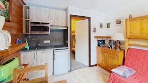 Un espacio habitable compacto con kitchenette, comedor y zona de estar con un sofá rojo.