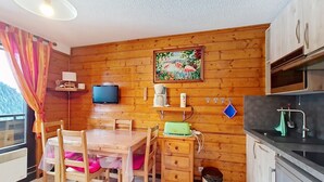 Una cocina compacta con paredes de madera, una mesa de comedor con sillas, un televisor montado sobre la mesa y un lavamanos pequeño.