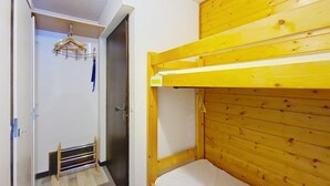 Una habitación pequeña y funcional con literas, una puerta que da a otra habitación y un perchero con ropa.
